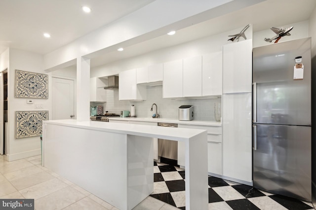 kitchen featuring wall chimney range hood, appliances with stainless steel finishes, white cabinetry, backsplash, and a center island