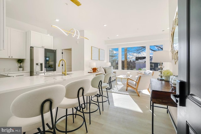 kitchen with pendant lighting, sink, white cabinetry, and stainless steel refrigerator with ice dispenser