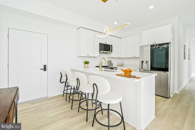 kitchen featuring white cabinetry, stainless steel appliances, decorative light fixtures, and light hardwood / wood-style flooring