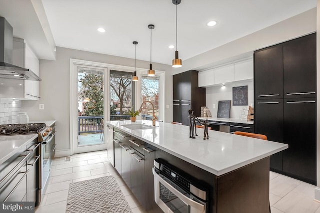 kitchen with wall chimney exhaust hood, dark brown cabinetry, sink, a center island with sink, and appliances with stainless steel finishes