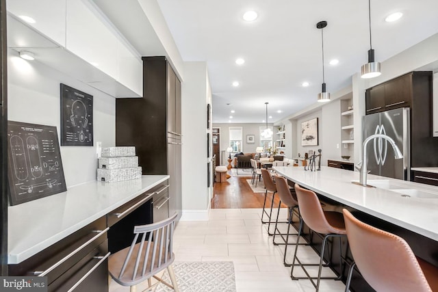 kitchen featuring stainless steel refrigerator, dark brown cabinetry, a kitchen bar, and white cabinets