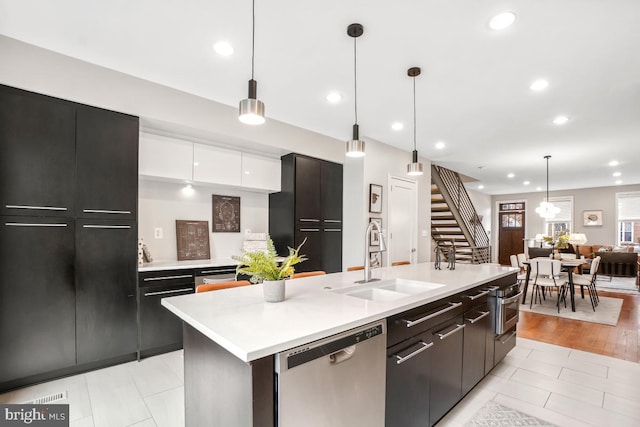 kitchen with pendant lighting, sink, white cabinetry, stainless steel appliances, and a center island with sink