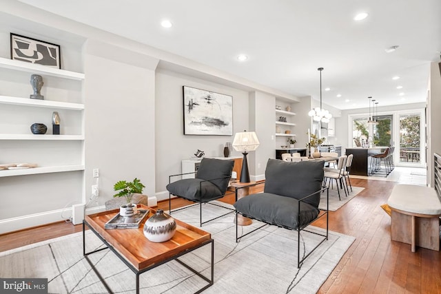 living room featuring an inviting chandelier, light wood-type flooring, and built in shelves