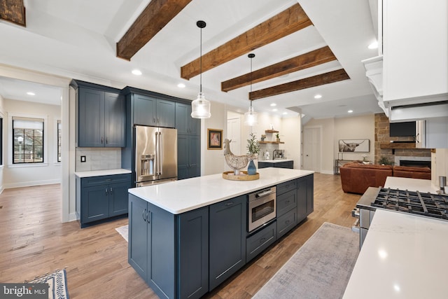 kitchen with backsplash, hanging light fixtures, stainless steel appliances, blue cabinetry, and light wood-type flooring