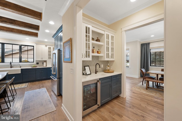 bar with white cabinetry, beverage cooler, high end fridge, and light wood-type flooring