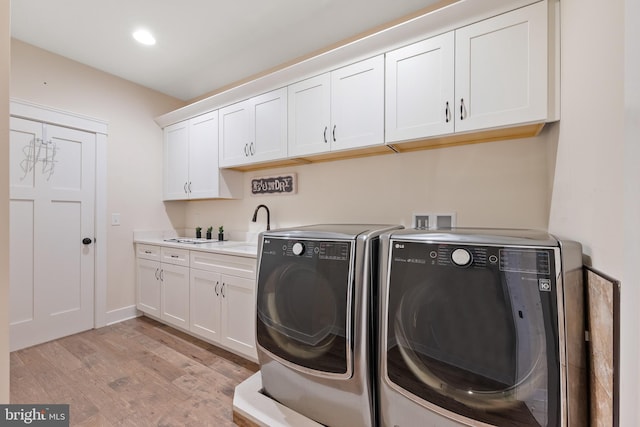 clothes washing area featuring cabinets, sink, washer and dryer, and light wood-type flooring