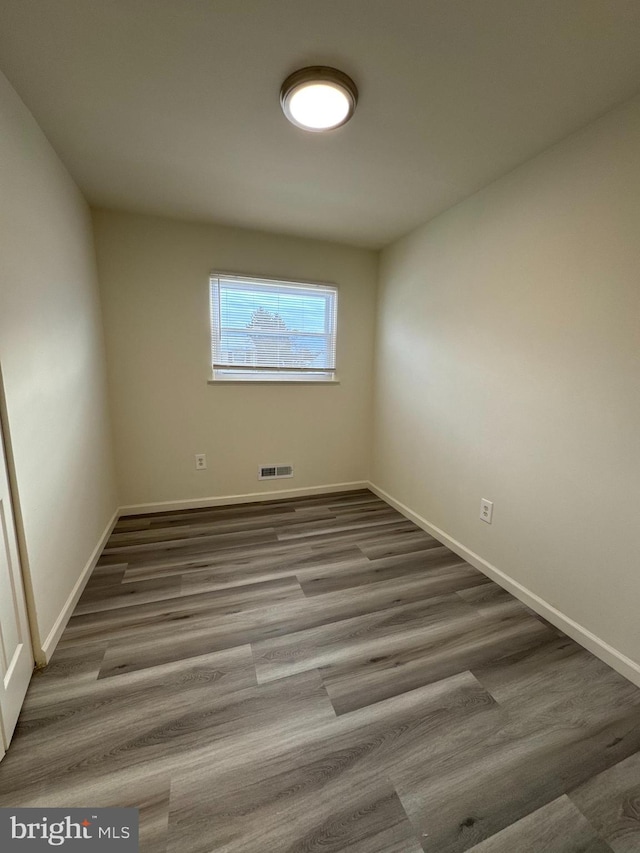 empty room with wood finished floors, visible vents, and baseboards