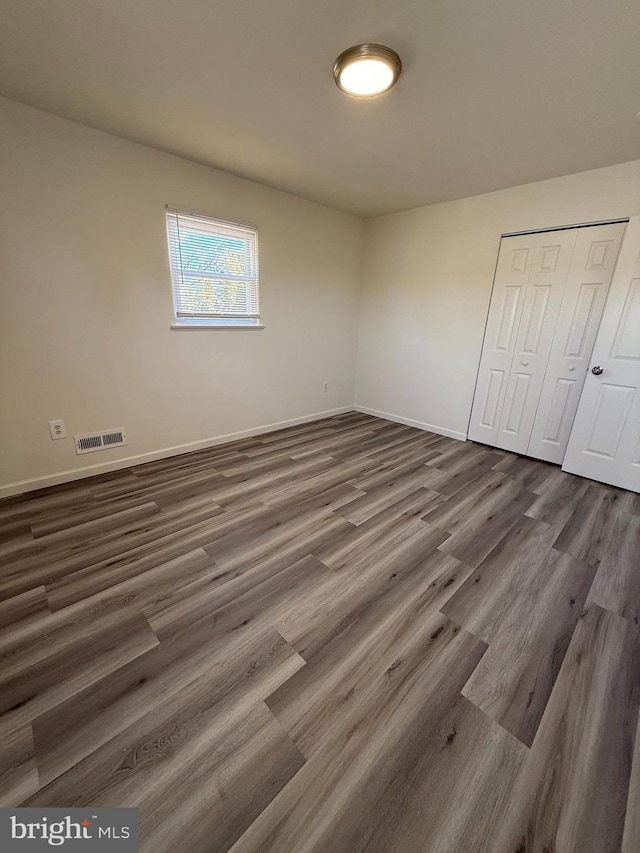 unfurnished bedroom with dark wood-type flooring, a closet, visible vents, and baseboards