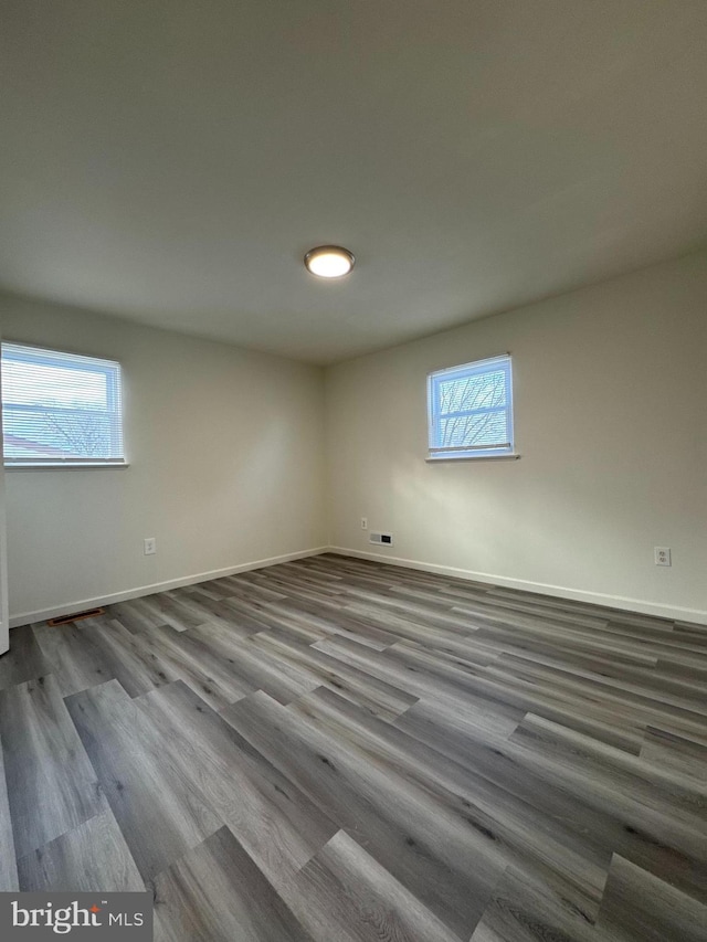 empty room featuring a healthy amount of sunlight, baseboards, and wood finished floors