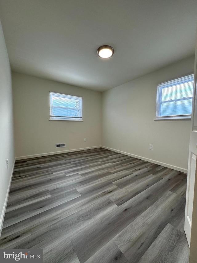 empty room with a wealth of natural light, visible vents, baseboards, and wood finished floors