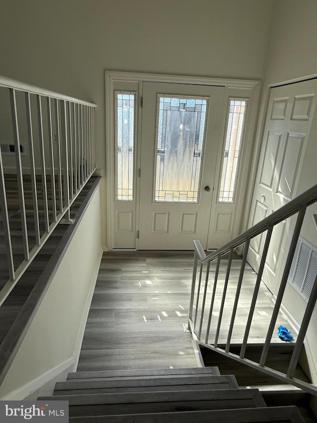 foyer featuring wood finished floors, visible vents, baseboards, and stairs