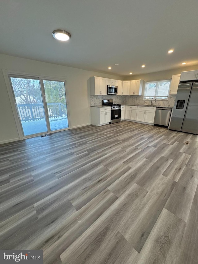 kitchen with white cabinets, decorative backsplash, light wood-style flooring, stainless steel appliances, and a sink