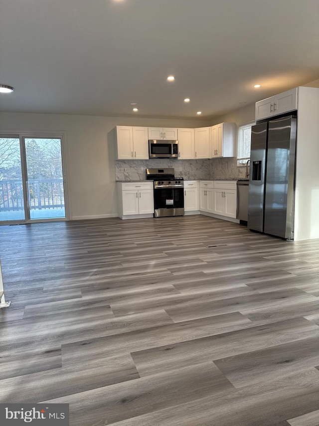 kitchen with appliances with stainless steel finishes, wood finished floors, white cabinetry, and decorative backsplash