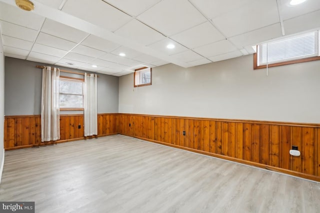 unfurnished room with a paneled ceiling, wooden walls, and light wood-type flooring