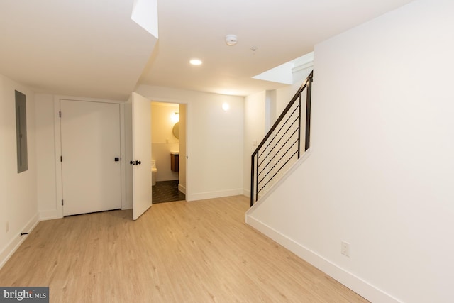 below grade area featuring electric panel, baseboards, stairway, light wood-type flooring, and recessed lighting