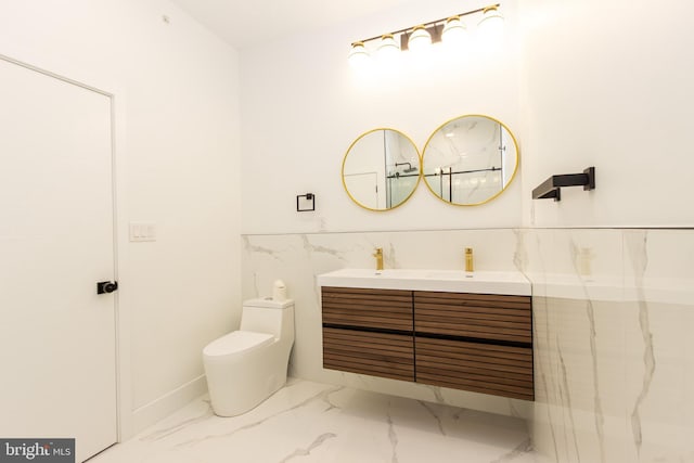 bathroom with toilet, a wainscoted wall, tile walls, marble finish floor, and double vanity