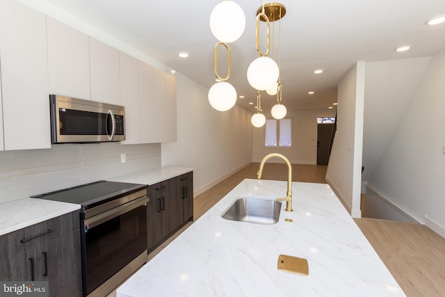 kitchen with light wood finished floors, appliances with stainless steel finishes, backsplash, and a sink