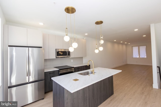 kitchen featuring appliances with stainless steel finishes, a sink, decorative light fixtures, and light wood-style floors