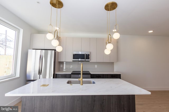 kitchen featuring a sink, appliances with stainless steel finishes, tasteful backsplash, modern cabinets, and a center island with sink