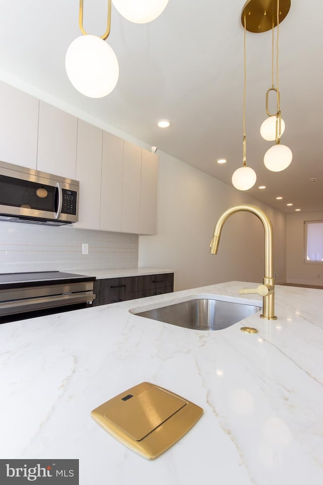 kitchen with decorative light fixtures, stainless steel microwave, backsplash, a sink, and light stone countertops