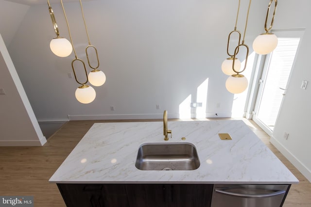 kitchen with wood finished floors, stainless steel dishwasher, a sink, and light stone countertops