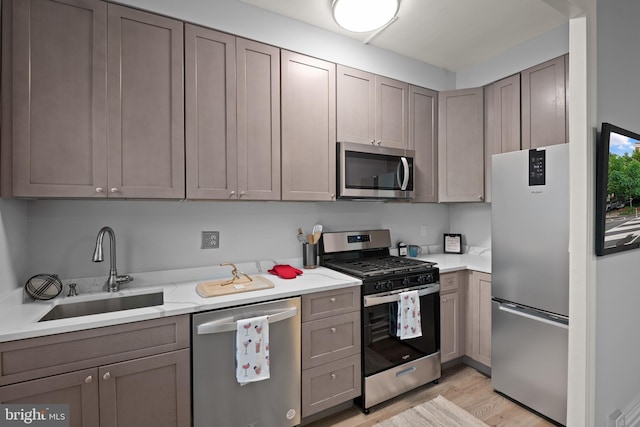 kitchen featuring stainless steel appliances, gray cabinets, sink, and light wood-type flooring