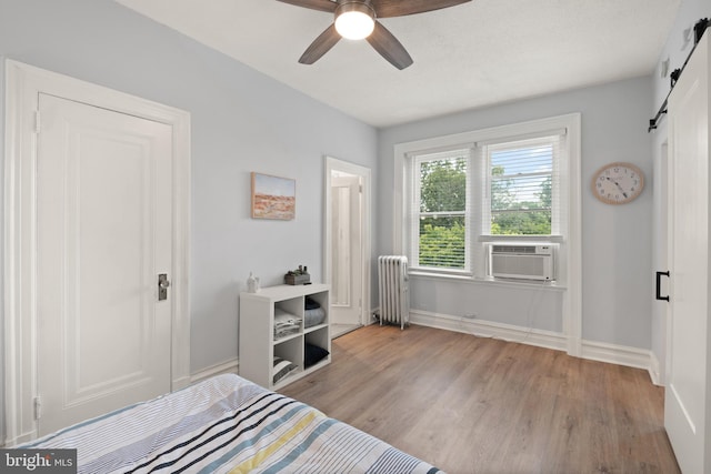 unfurnished bedroom with radiator heating unit, cooling unit, ceiling fan, light hardwood / wood-style floors, and a barn door