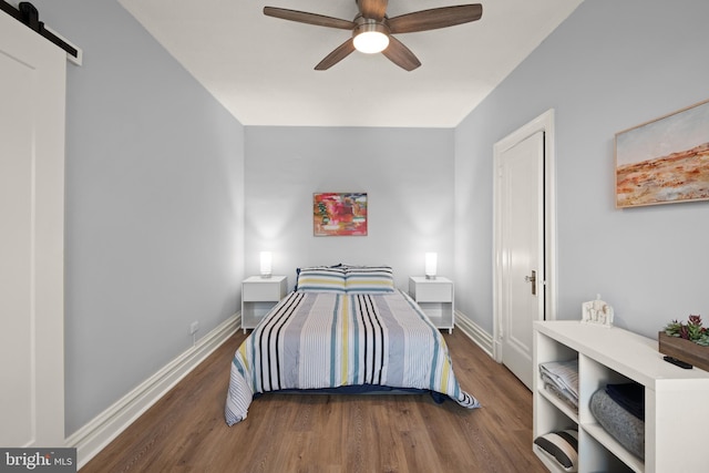 bedroom with dark hardwood / wood-style floors, a barn door, and ceiling fan