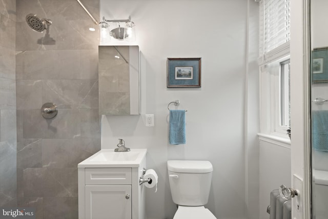 bathroom with tiled shower, vanity, toilet, and radiator