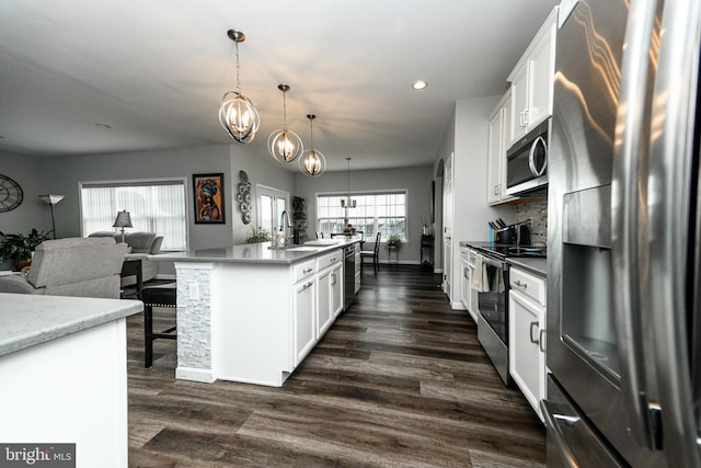 kitchen with appliances with stainless steel finishes, hanging light fixtures, a center island with sink, and white cabinets