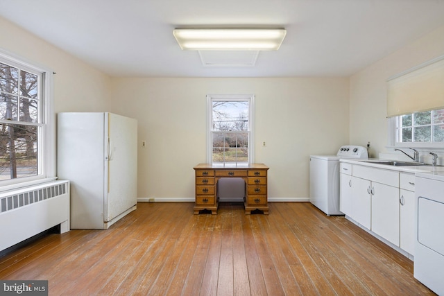 laundry area with radiator heating unit, washer / dryer, sink, and light hardwood / wood-style flooring