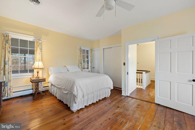 bedroom with ceiling fan, hardwood / wood-style floors, baseboard heating, and a closet