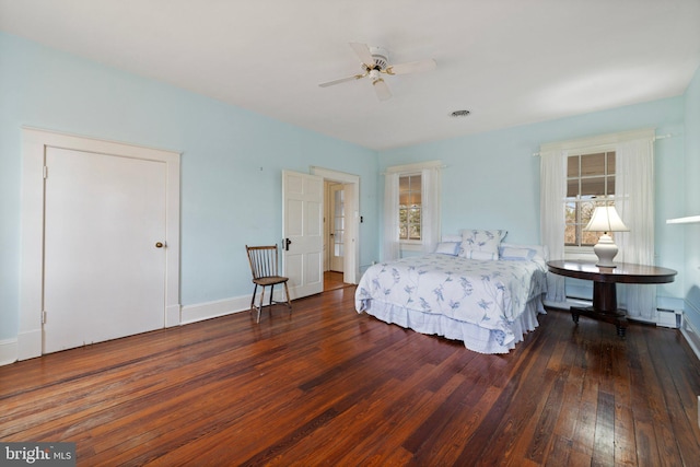 bedroom featuring ceiling fan, dark hardwood / wood-style floors, multiple windows, and a baseboard radiator