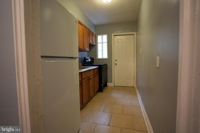 kitchen featuring black electric range oven, light tile patterned floors, and white refrigerator