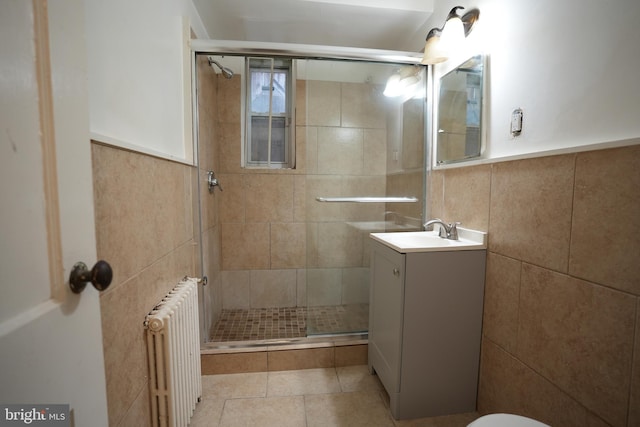 bathroom with a shower with shower door, tile walls, radiator heating unit, vanity, and tile patterned flooring