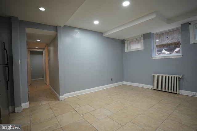 basement featuring radiator, light tile patterned floors, and refrigerator