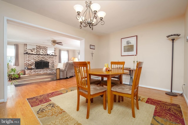 dining room with ceiling fan with notable chandelier, hardwood / wood-style floors, and a brick fireplace