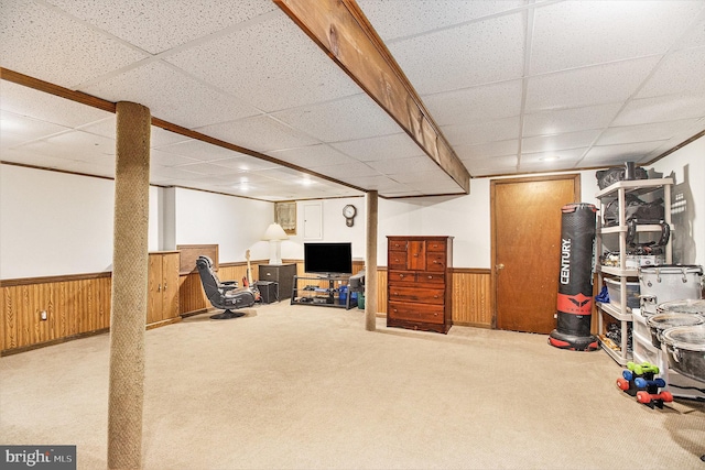 basement featuring a paneled ceiling, light colored carpet, and wood walls