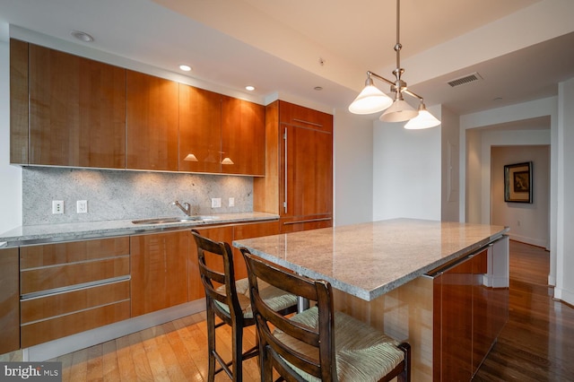 kitchen with light stone counters, sink, hanging light fixtures, and a kitchen island