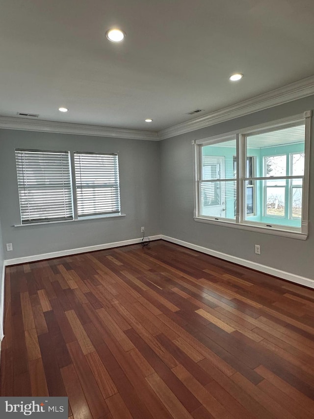 spare room with baseboards, dark wood finished floors, visible vents, and crown molding