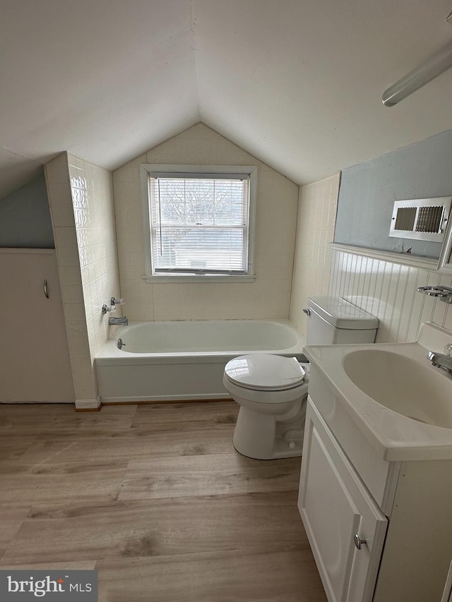 full bath with toilet, a bath, wood finished floors, and lofted ceiling