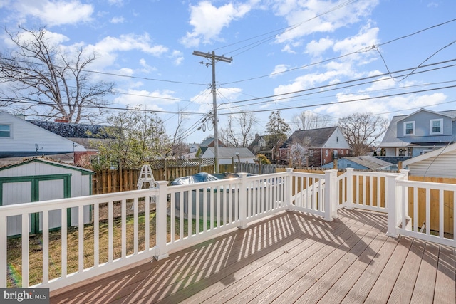 wooden deck with a residential view, fence, a storage unit, and an outbuilding