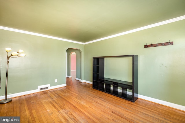 spare room with ornamental molding, arched walkways, baseboards, and wood finished floors