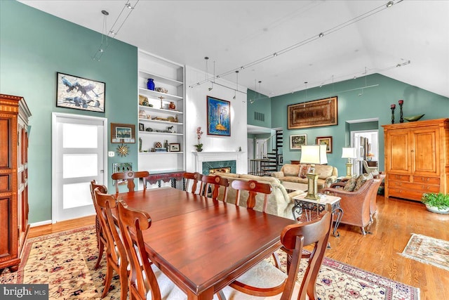 dining area featuring high vaulted ceiling, built in shelves, a high end fireplace, and light hardwood / wood-style floors