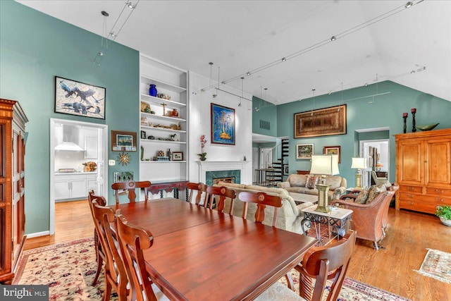 dining space featuring high vaulted ceiling, a high end fireplace, built in features, and light hardwood / wood-style floors