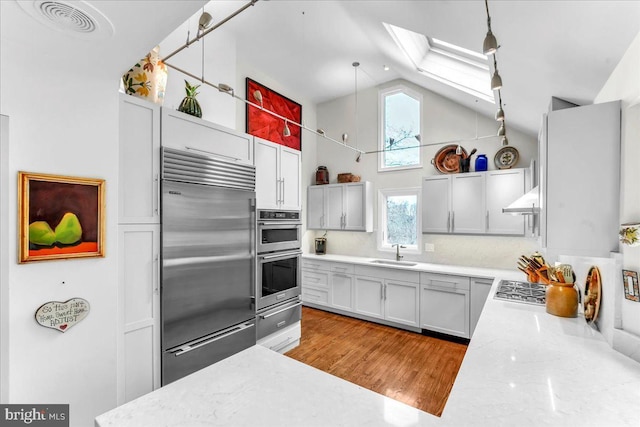 kitchen with sink, hanging light fixtures, a skylight, stainless steel appliances, and high vaulted ceiling