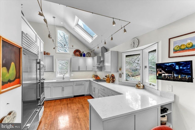 kitchen featuring wall chimney range hood, sink, appliances with stainless steel finishes, a skylight, and kitchen peninsula