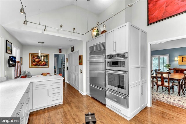 kitchen with decorative light fixtures, high vaulted ceiling, light hardwood / wood-style flooring, appliances with stainless steel finishes, and white cabinets