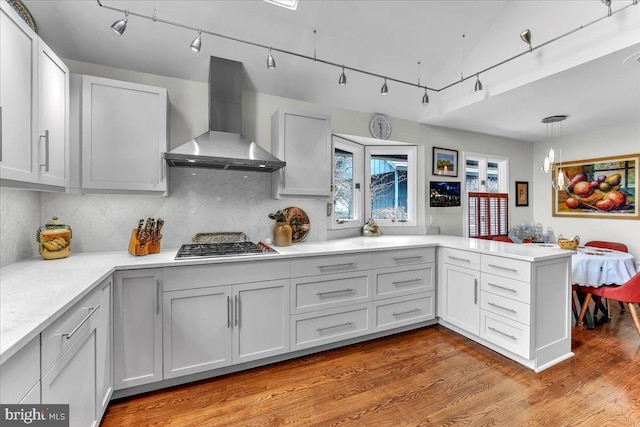 kitchen with hardwood / wood-style floors, pendant lighting, white cabinetry, kitchen peninsula, and wall chimney exhaust hood