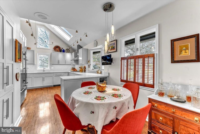 dining room with sink, vaulted ceiling with skylight, and light hardwood / wood-style floors